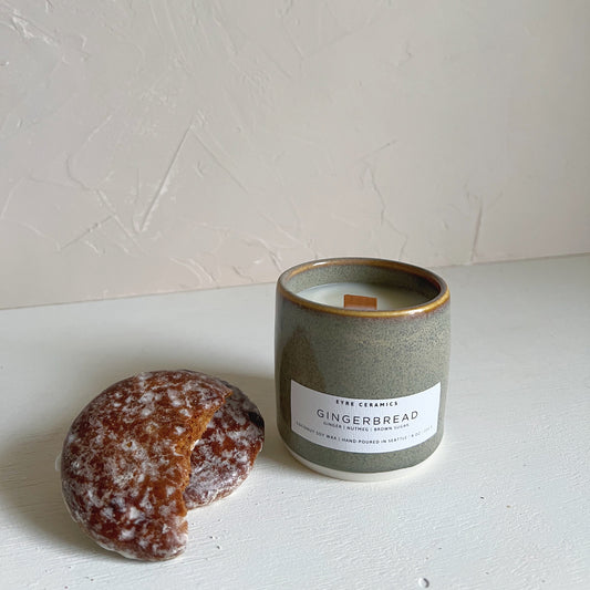 Candle labeled 'Gingerbread' next to a gingerbread cookie on a light surface with a white background