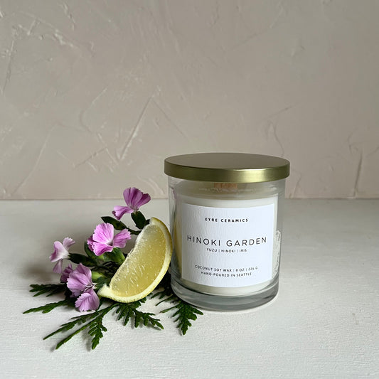 Candle labeled 'Hinoki Garden' with a slice of lemon and flowers on a light background
