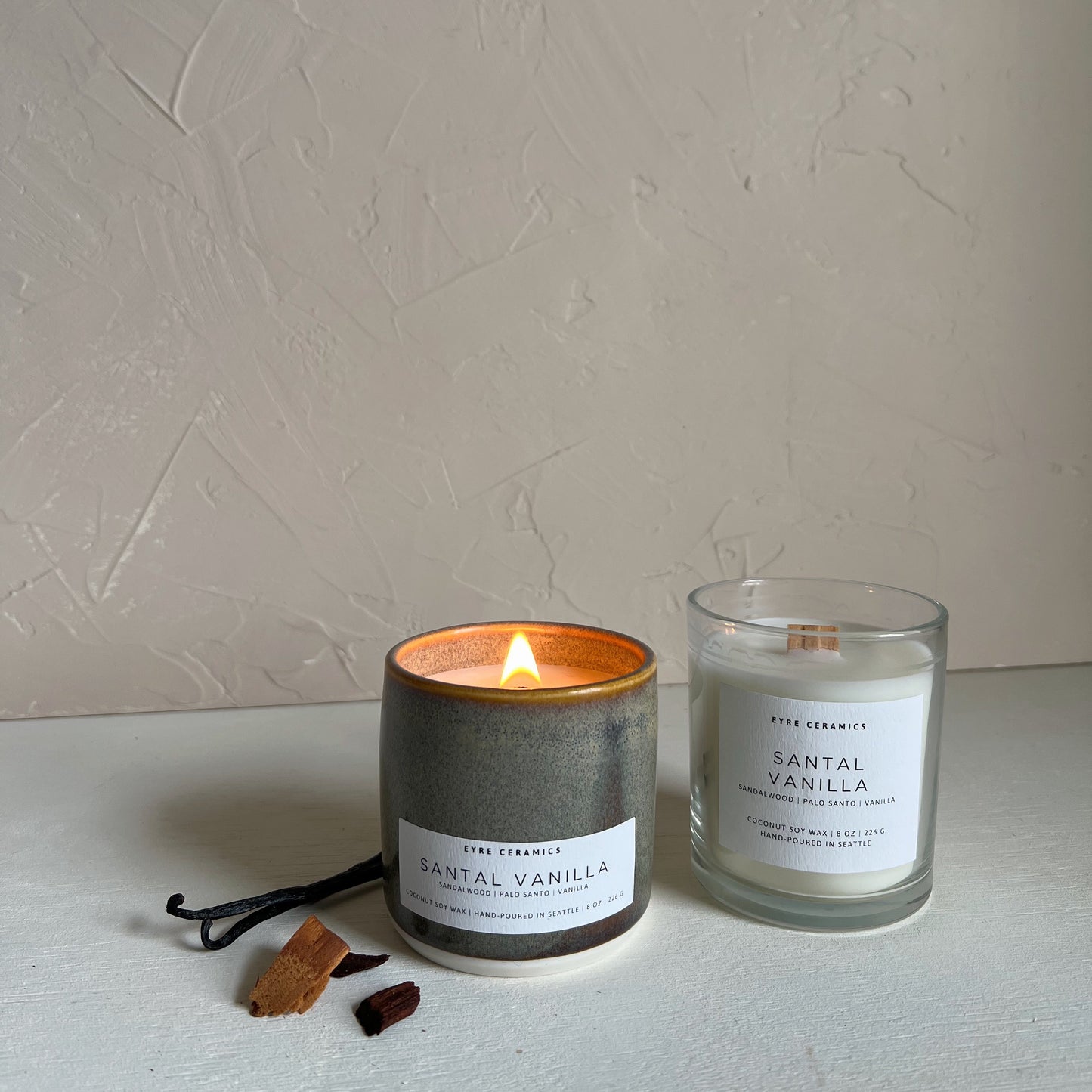 Two candles labeled 'Santal Vanilla' on a light surface with a neutral background