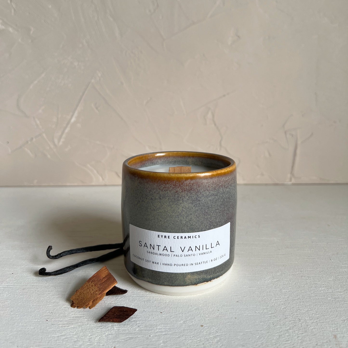 Candle labeled 'Santal Vanilla' with vanilla beans and a pod on a neutral background