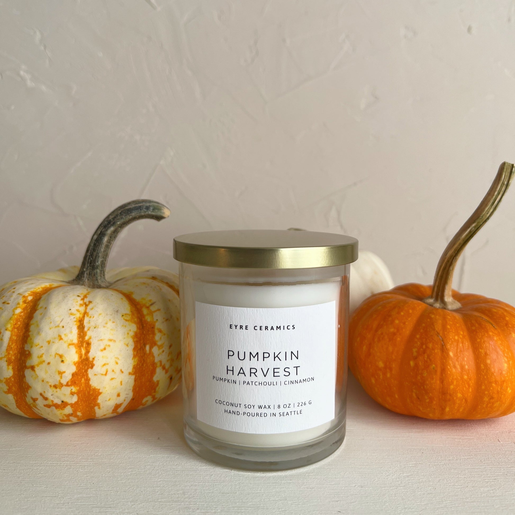 Candle labeled 'Pumpkin Harvest' with two small pumpkins on a neutral background