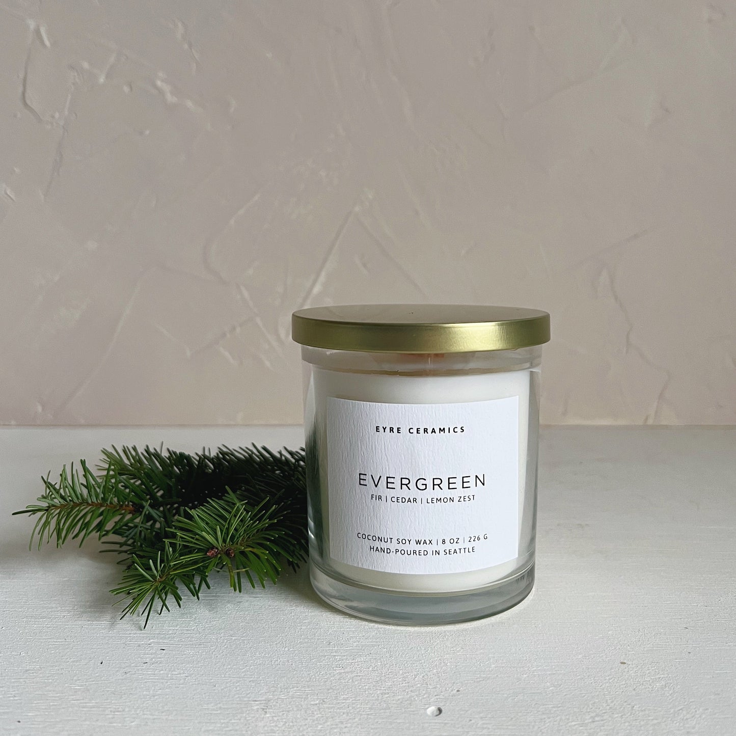 Candle jar labeled 'Evergreen' with a gold lid on a light surface.