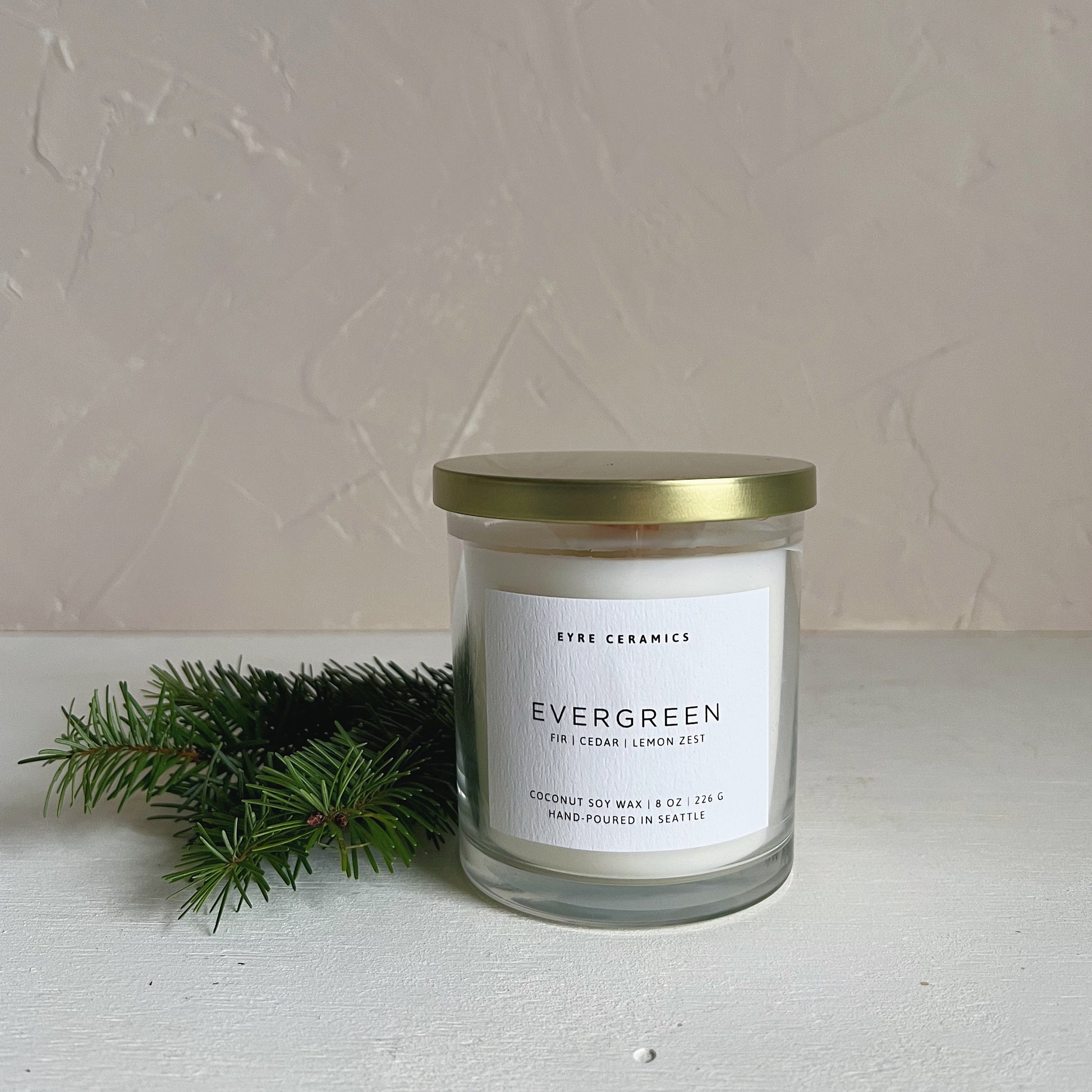 Candle jar labeled 'Evergreen' with a gold lid on a light surface.