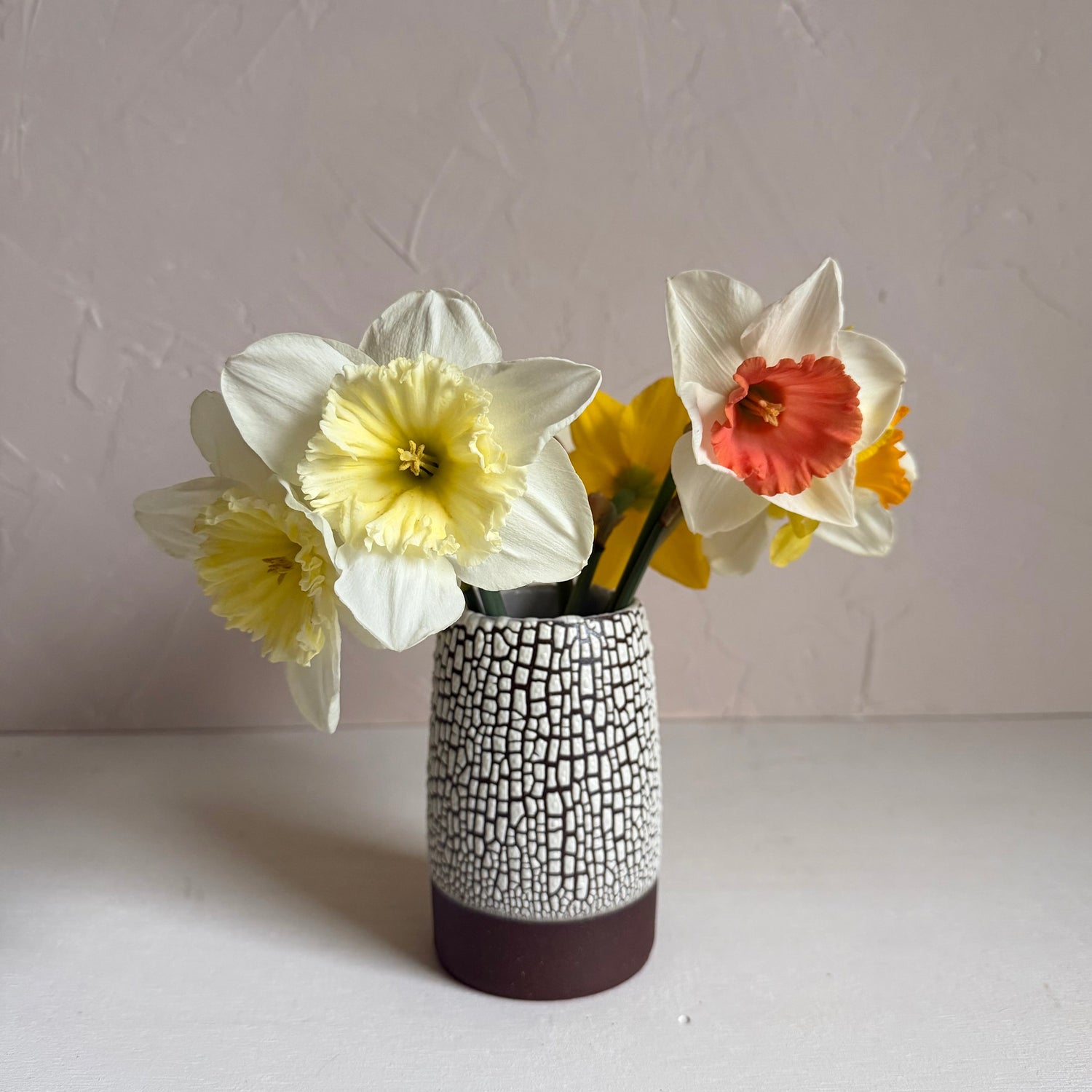 Decorative vase with a textured pattern containing flowers on a plain background