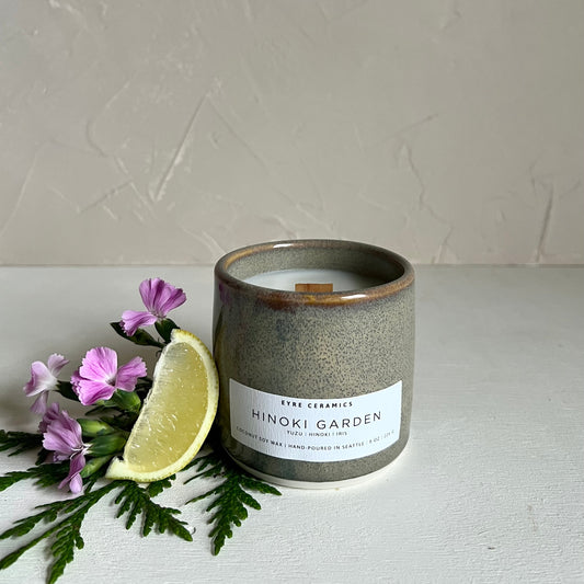 Candle labeled 'Hinoki Garden' with a slice of lime and flowers on a white surface.