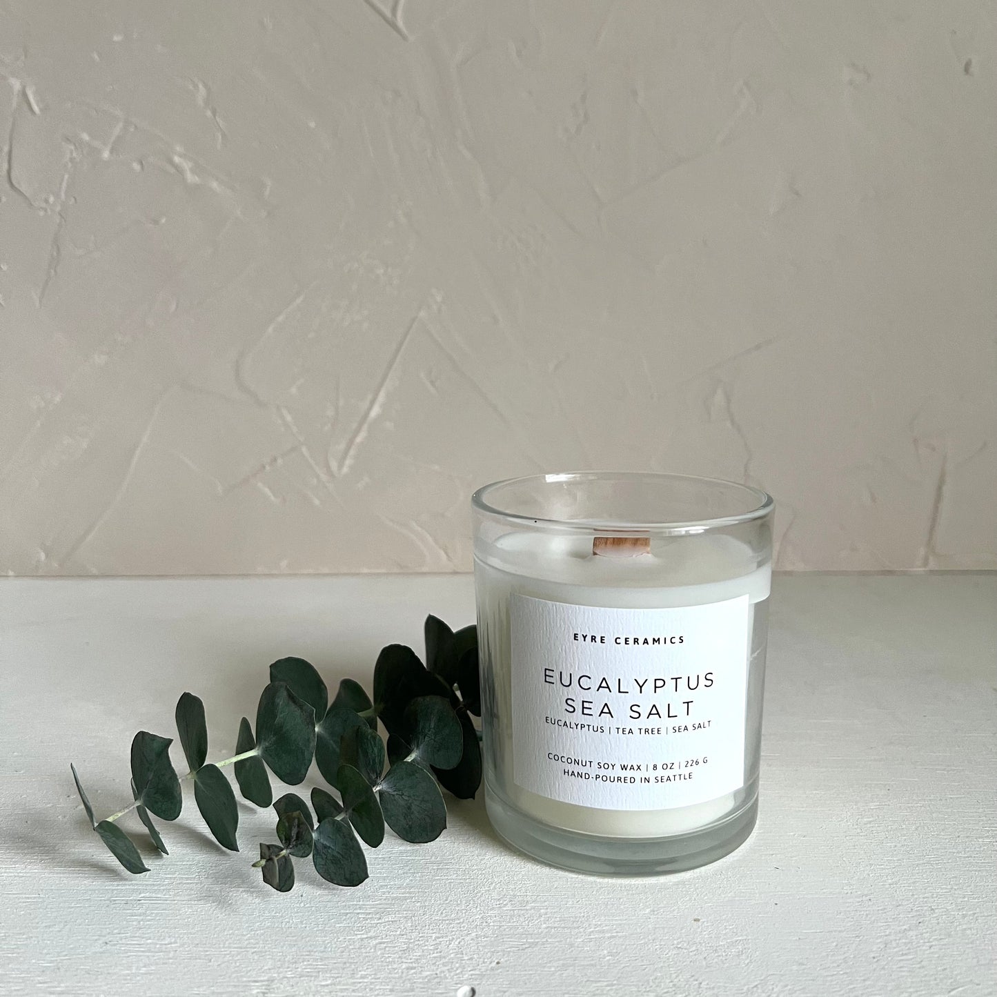 Candle labeled 'Eucalyptus Sea Salt' with eucalyptus leaves on a neutral background