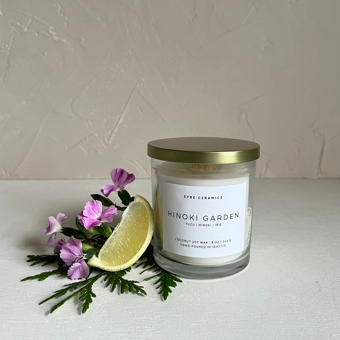Candle labeled 'Hinoki Garden' with a slice of lemon and flowers on a light background