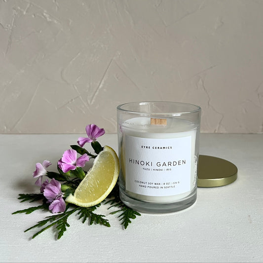 Candle labeled 'Hinoki Garden' with flowers and a lime wedge on a white surface.