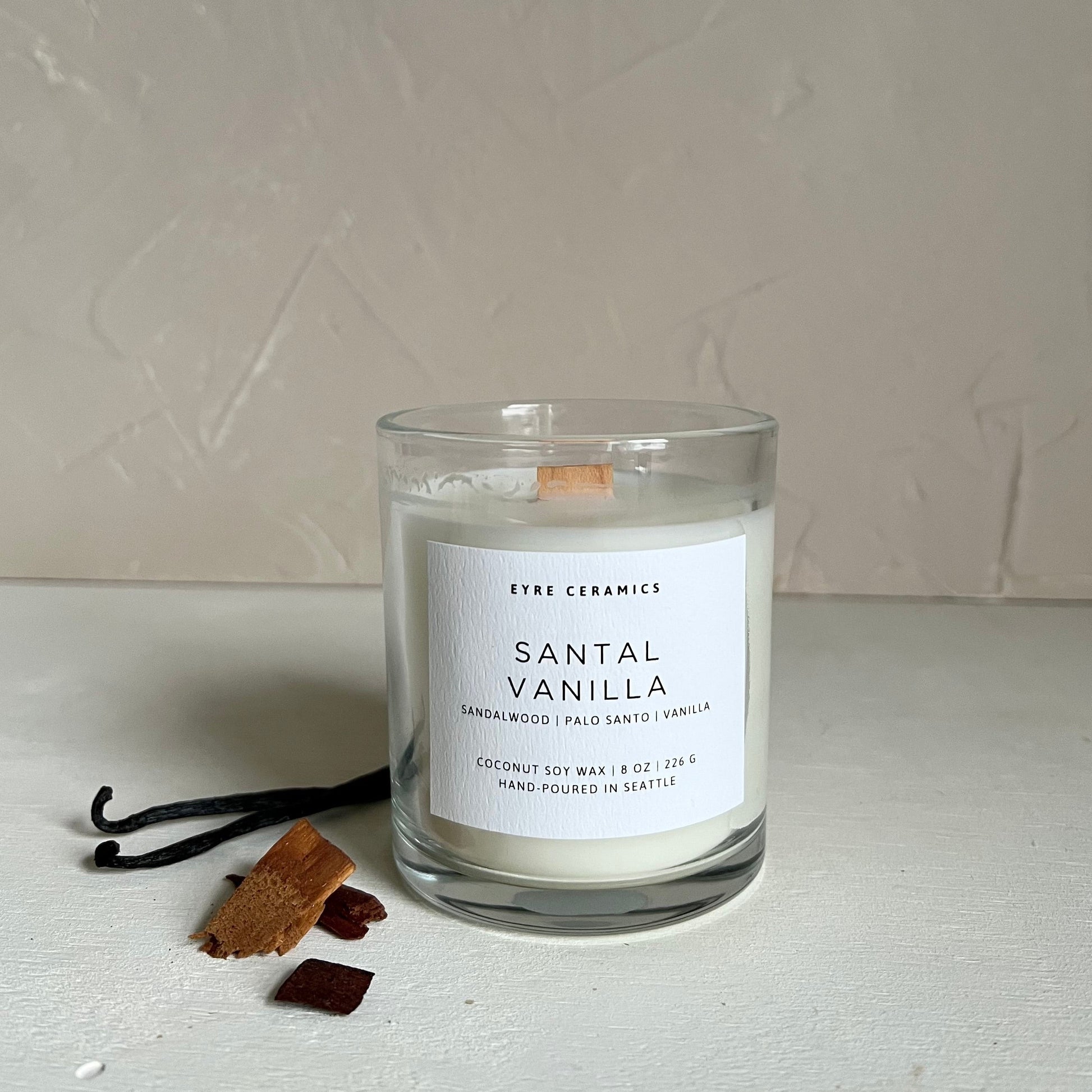 Candle labeled 'Santal Vanilla' with vanilla beans and a vanilla pod on a light background