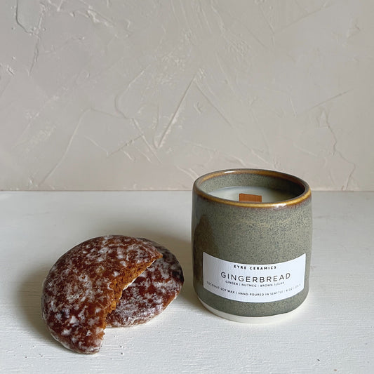Candle labeled 'Gingerbread' next to a gingerbread cookie on a light surface with a neutral background