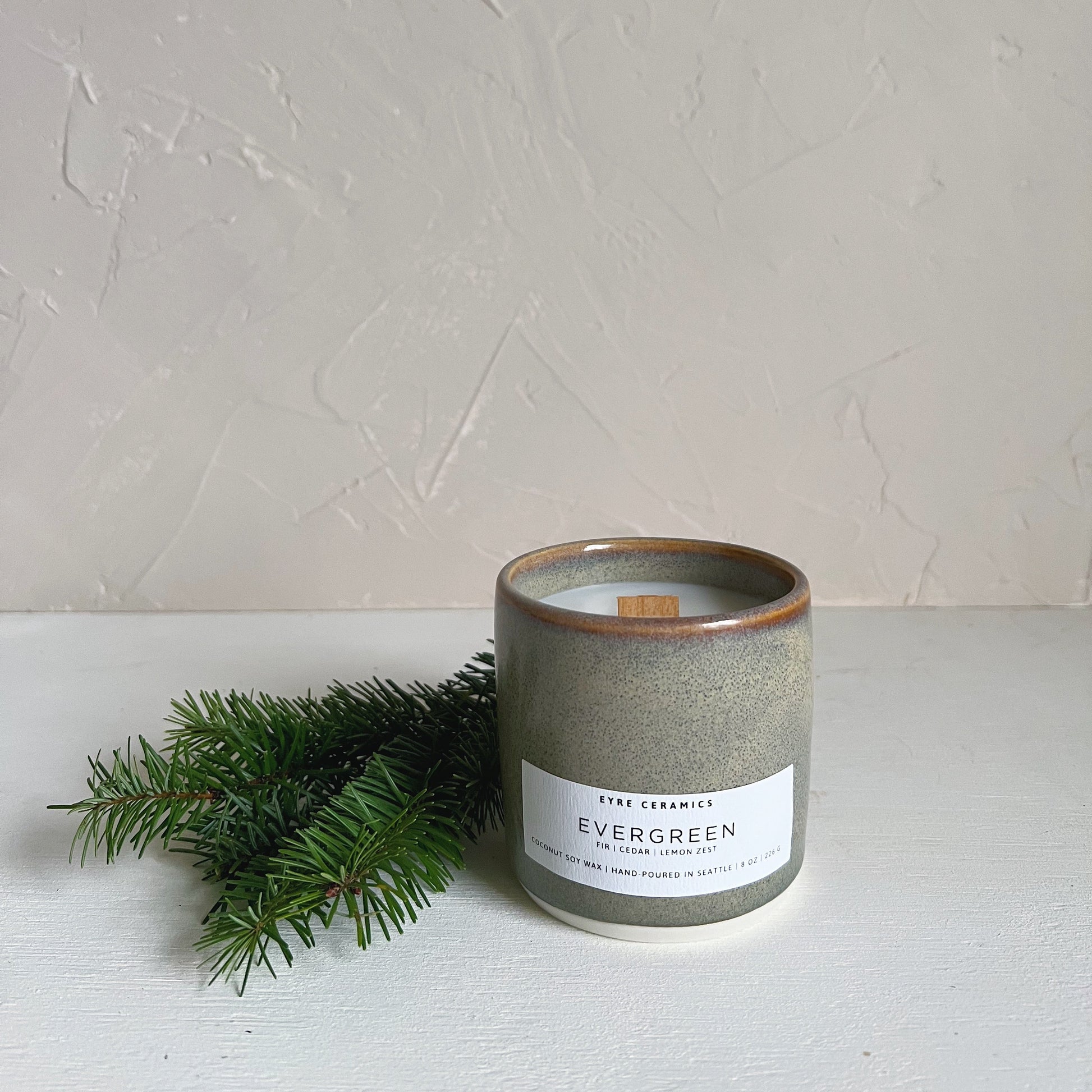 Ceramic candle labeled 'Evergreen' with a small branch on a light background