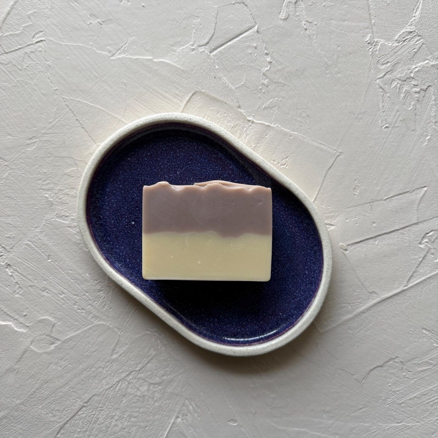 Bar of soap on a purple ceramic dish with a white background