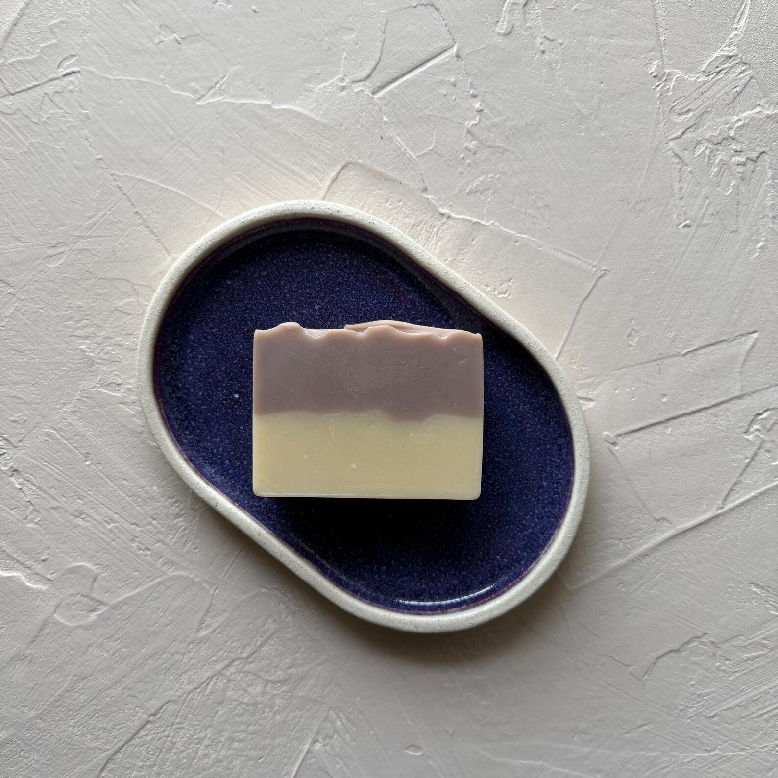 Bar of soap on a purple ceramic dish with a white background