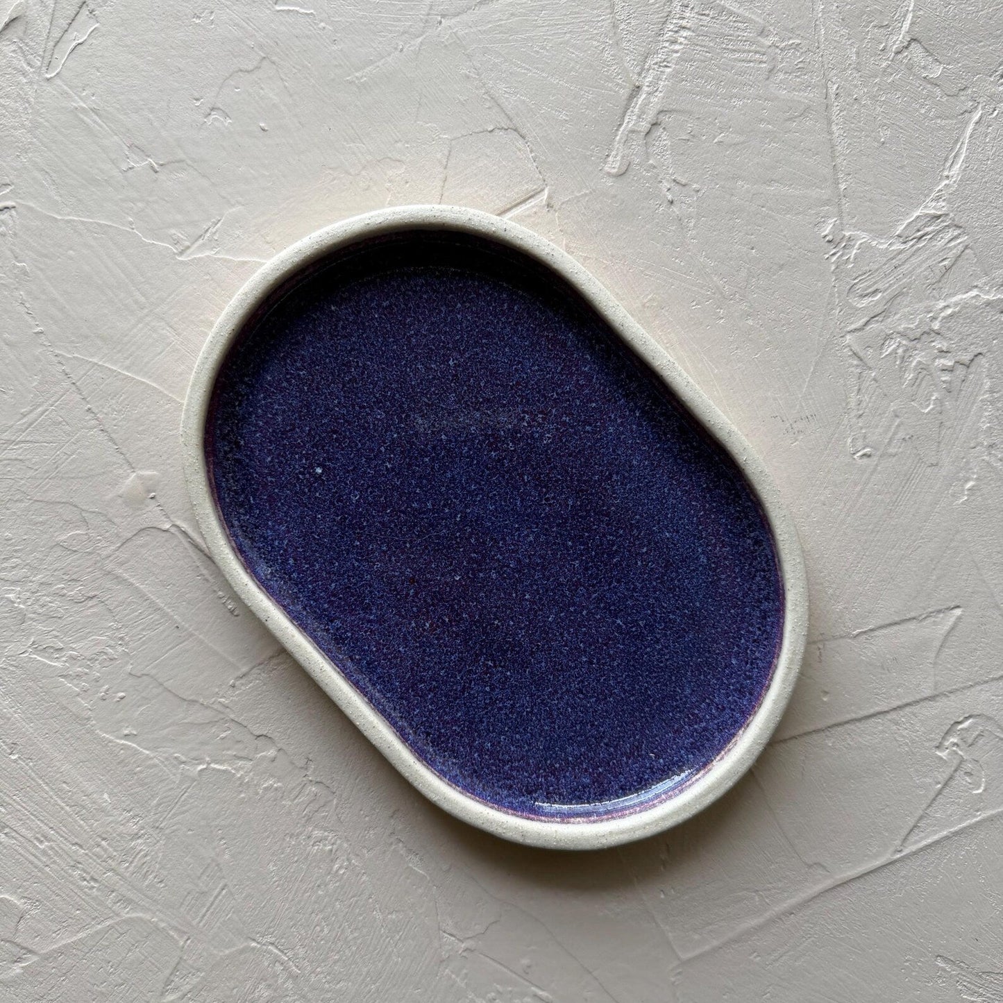 Oval ceramic dish with purple interior on a gray textured surface