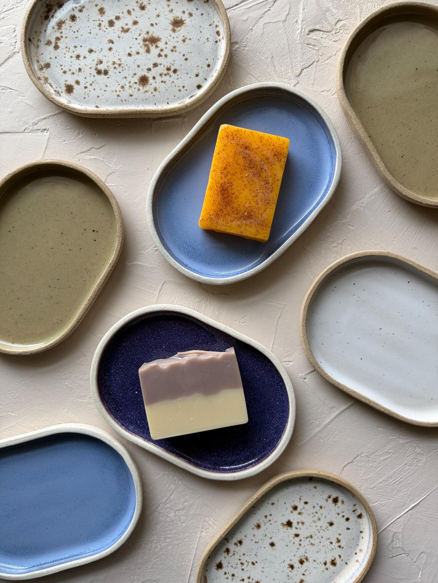 Collection of ceramic plates with soap and a bar of soap on a textured surface